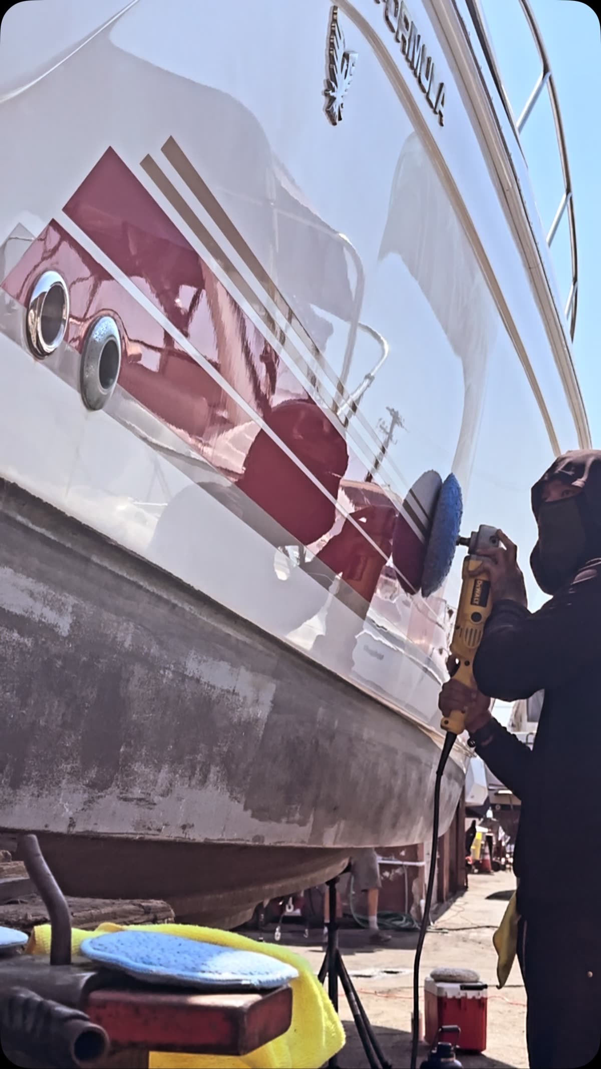 Polishing a red-striped hull on stands in the boatyard